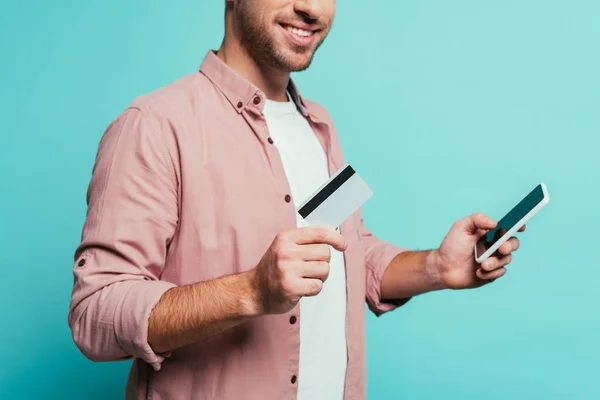 Vista cortada de homem compras on-line com smartphone e cartão de crédito, isolado em azul — Fotografia de Stock