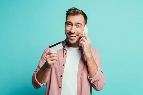 Homem sorrindo compras on-line com smartphone e cartão de crédito, isolado em azul — Fotografia de Stock