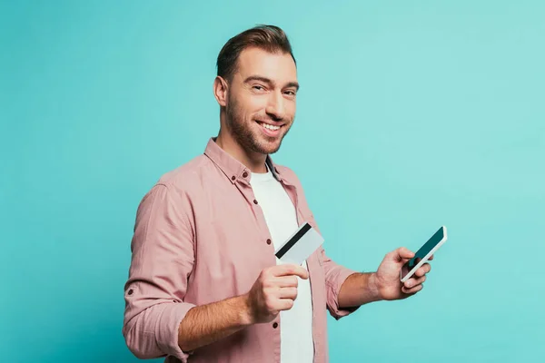 Cheerful bearded man shopping online with smartphone and credit card, isolated on blue — Stock Photo