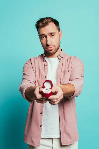 Frustrated man holding box with proposal ring, isolated on blue — Stock Photo