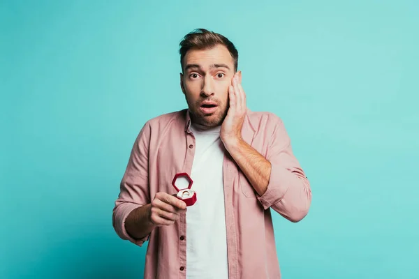 Homme effrayé tenant boîte avec bague de proposition, isolé sur bleu — Photo de stock