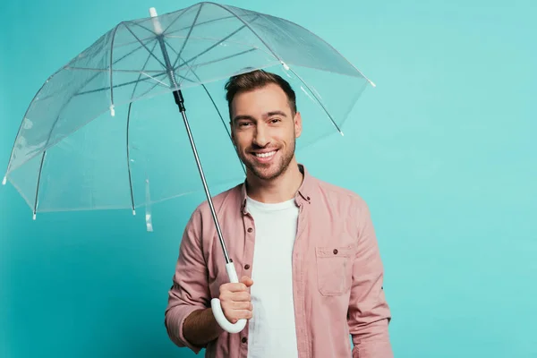 Uomo barbuto sorridente che tiene l'ombrello, isolato sul blu — Foto stock