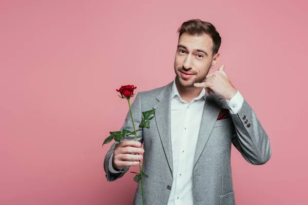 Uomo barbuto in giacca e cravatta con fiore rosa e mostrandomi chiamami gesto, isolato su rosa — Foto stock