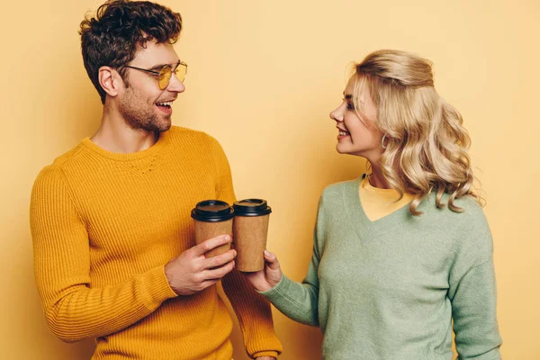 Happy man and woman looking at each other while clinking with paper cups on yellow background — Stock Photo