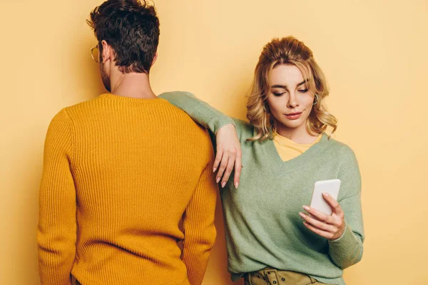 Back view of man standing near pretty girl using smartphone on yellow background — Stock Photo