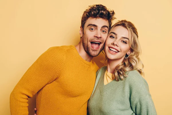 Joven, alegre pareja abrazándose mientras sonríe a la cámara sobre fondo amarillo - foto de stock