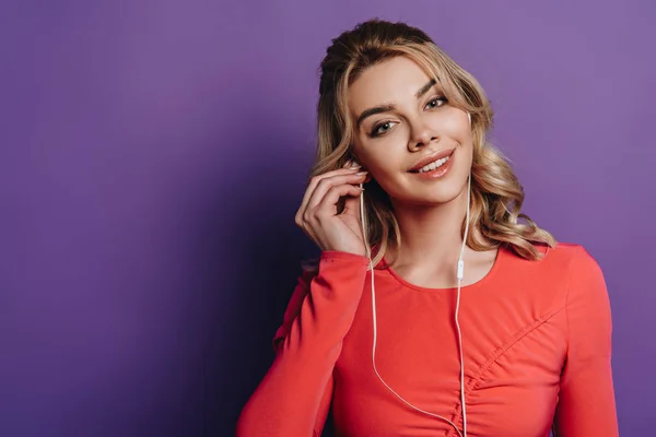 Smiling girl listening music in earphones and looking at camera on purple background — Stock Photo