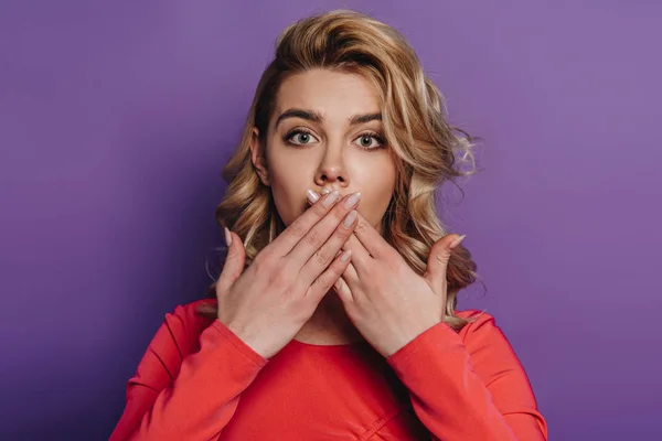 Shocked girl covering mouth with hands while looking at camera on purple background — Stock Photo