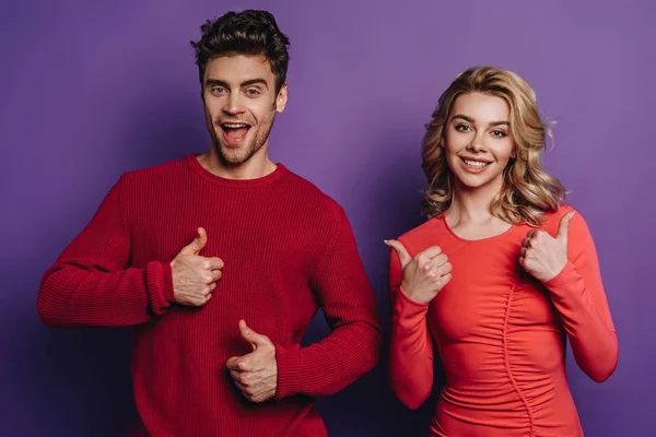 Happy couple showing thumbs up while looking at camera on purple background — Stock Photo