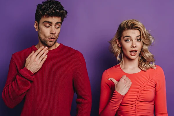 Schockiertes Mädchen zeigt mit Daumen auf entmutigten Freund auf lila Hintergrund — Stockfoto