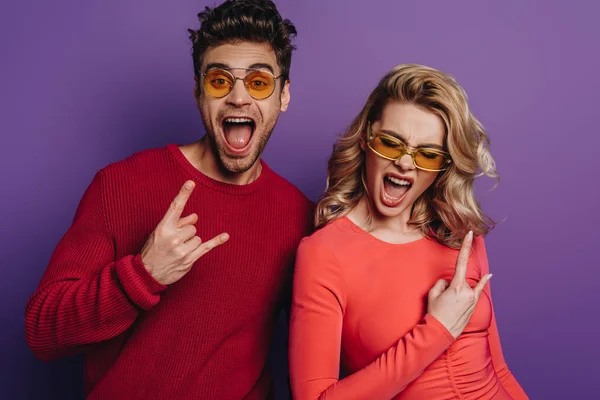 Excité homme et femme montrant des signes de roche sur fond violet — Photo de stock