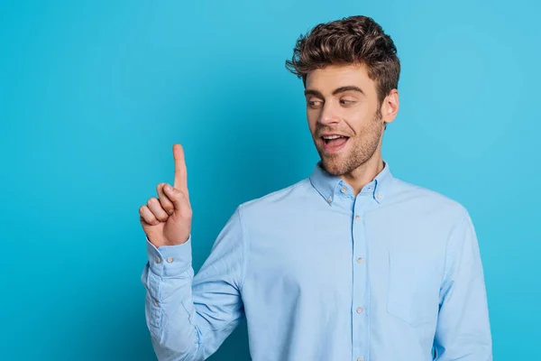 Positiver Mann lächelt und zeigt Ideengeste auf blauem Hintergrund — Stockfoto