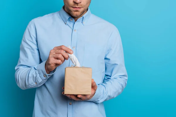 Vue recadrée de jeune homme contrarié prenant serviette en papier de paquet sur fond bleu — Photo de stock