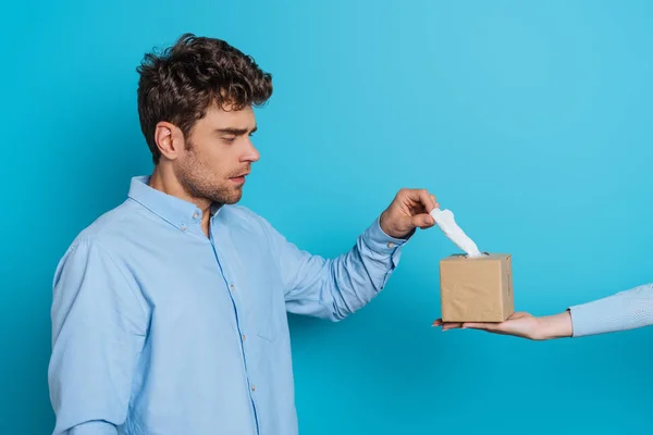 Partial view of woman giving pack of paper napkins to sad man on blue background — Stock Photo