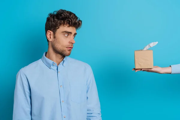 Visão cortada de mulher dando pacote de guardanapos de papel para perturbar o homem no fundo azul — Fotografia de Stock