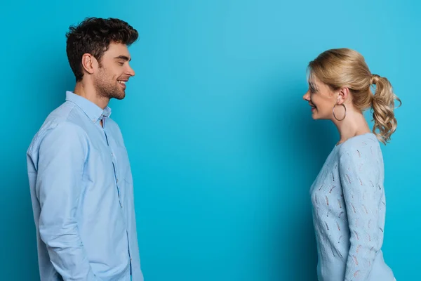 Vista lateral del hombre y la mujer felices sonriéndose el uno al otro sobre fondo azul - foto de stock
