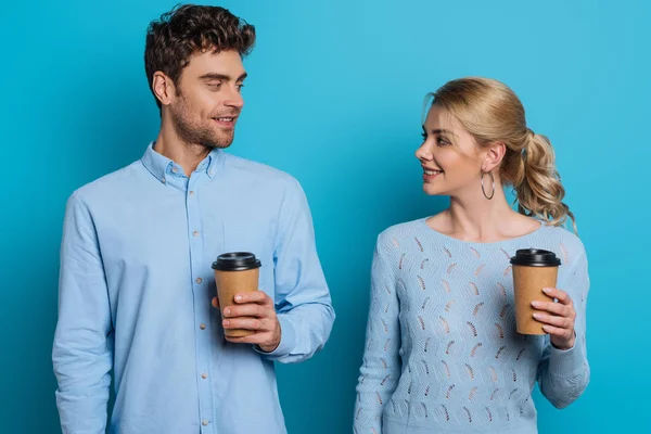 Smiling man and woman holding disposable cups while looking at each other on blue background — Stock Photo