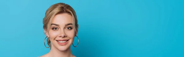 Panoramic shot of attractive, cheerful girl smiling at camera on blue background — Stock Photo