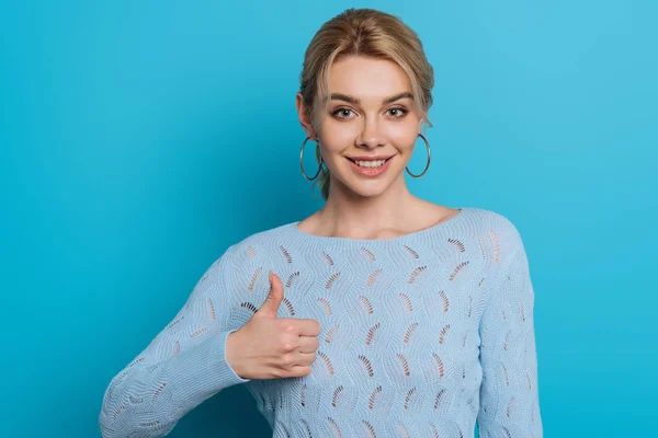 Happy girl showing thumb up while smiling at camera on blue background — Stock Photo