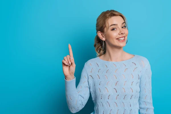 Beautiful girl smiling at camera while showing idea sign on blue background — Stock Photo