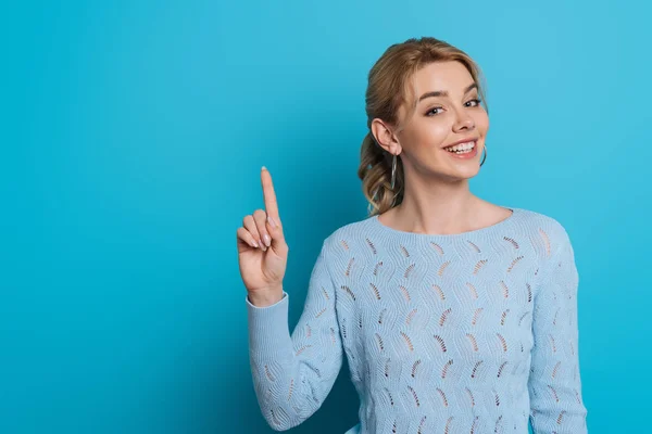 Schönes Mädchen lächelt in die Kamera, während es Ideenschild auf blauem Hintergrund zeigt — Stockfoto