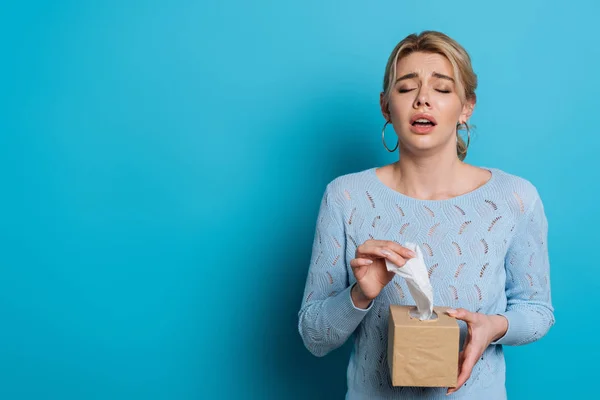 Crying girl holding pack of paper napkins on blue background — Stock Photo