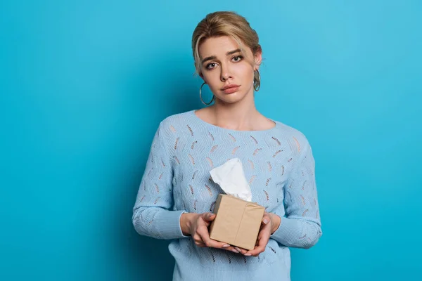 Ofendido chica sosteniendo paquete de servilletas de papel mientras mira a la cámara en fondo azul - foto de stock