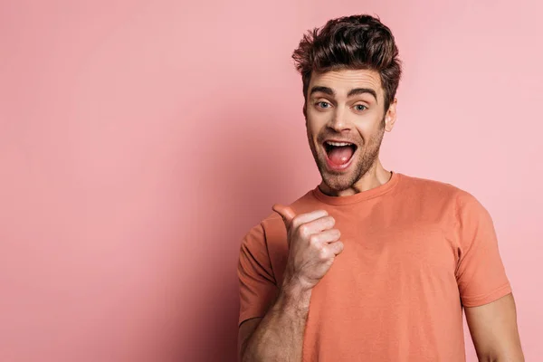 Excited man pointing with thumb while looking at camera on pink background — Stock Photo