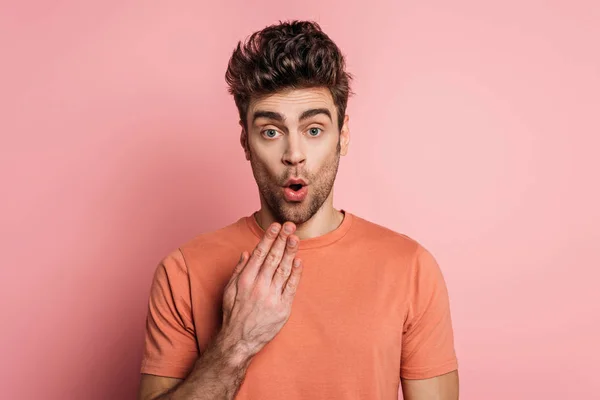 Shocked man holding hand near mouth while looking at camera on pink background — Stock Photo