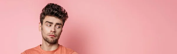 Panoramic shot of offended young man looking away on pink background — Stock Photo