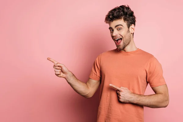 Amazed young man pointing with fingers while looking at camera on pink background — Stock Photo