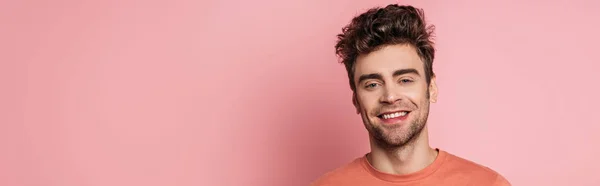 Panoramic shot of happy young man smiling at camera on pink background — Stock Photo