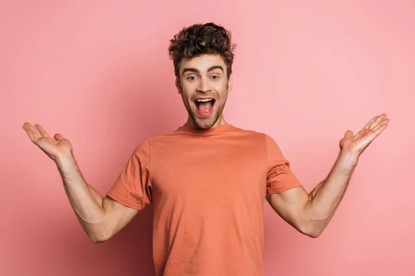 Excited young man laughing at camera while standing with open arms on pink background — Stock Photo