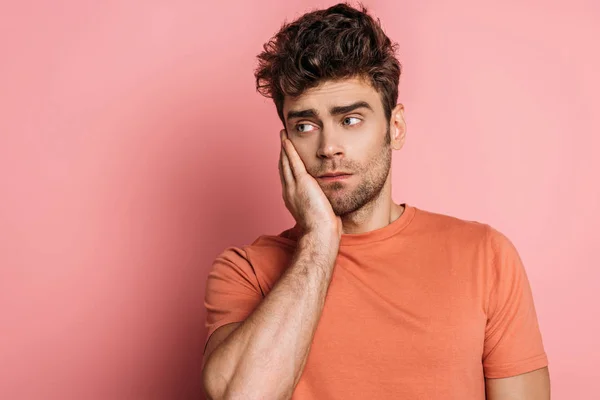 Bouleversé jeune homme toucher poussin tout en souffrant de mal de dents sur fond rose — Photo de stock