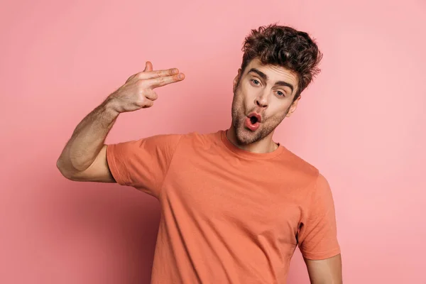 Young man imitating self-killing by shooting on pink background — Stock Photo