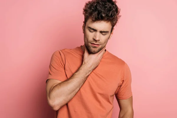 Sick young man with closed eyes touching throat on pink background — Stock Photo