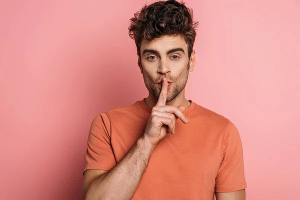 Handsome man showing hush sign while looking at camera on pink background — Stock Photo