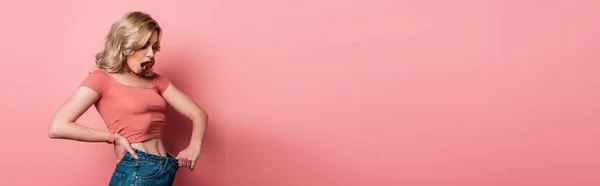 Plan panoramique de fille choquée portant un jean surdimensionné sur fond rose — Photo de stock