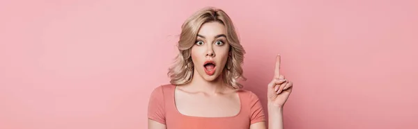 Foto panorámica de la chica sorprendida mostrando signo de idea mientras mira a la cámara en el fondo rosa - foto de stock