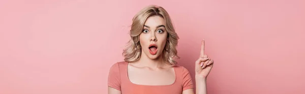 Panoramic shot of surprised girl showing idea sign while looking at camera on pink background — Stock Photo