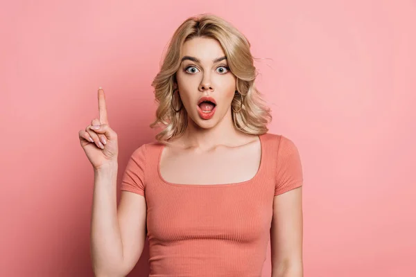 Surprised girl showing idea sign while looking at camera on pink background — Stock Photo