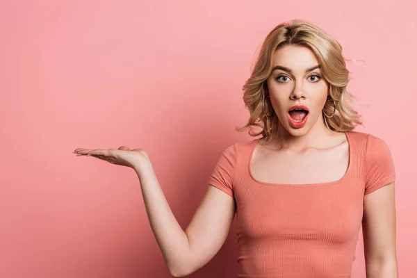 Chica sorprendida señalando con la mano mientras mira a la cámara en el fondo rosa — Stock Photo