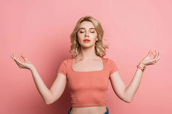 Pretty girl meditating with closed eyes while standing on pink background — Stock Photo