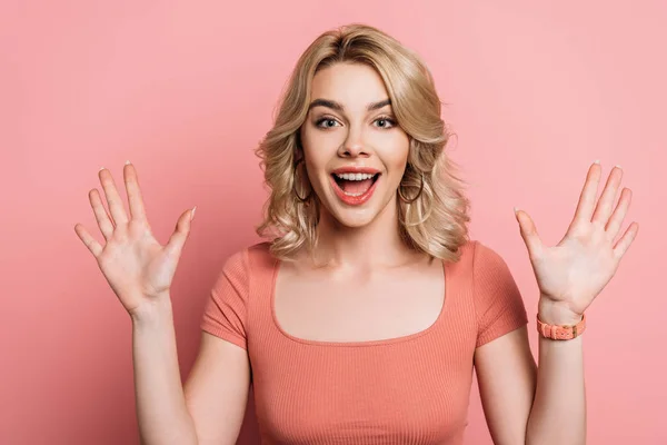 Alegre chica agitando las manos mientras sonríe a la cámara en el fondo rosa - foto de stock