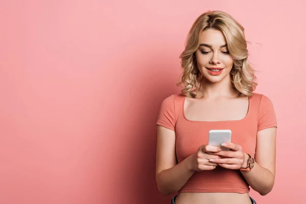 Bella, sorridente ragazza chatta su smartphone su sfondo rosa — Foto stock