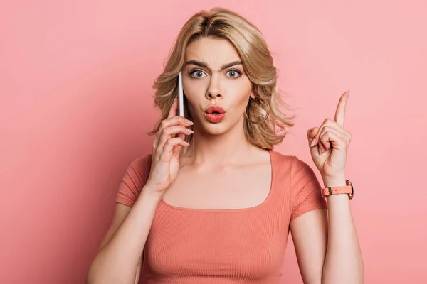 Shocked girl showing idea gesture while talking on smartphone on pink background — Stock Photo