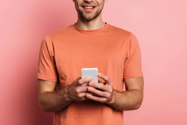 Vista recortada del hombre sonriente utilizando el teléfono inteligente sobre fondo rosa - foto de stock