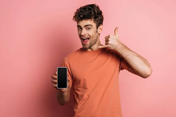 Alegre joven mostrando deja beber gesto mientras sostiene el teléfono inteligente con pantalla en blanco sobre fondo rosa - foto de stock