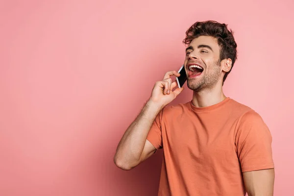 Alegre joven riendo mientras habla en el teléfono inteligente sobre fondo rosa - foto de stock