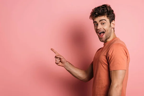 Excited young man pointing with finger while looking at camera on pink background — Stock Photo